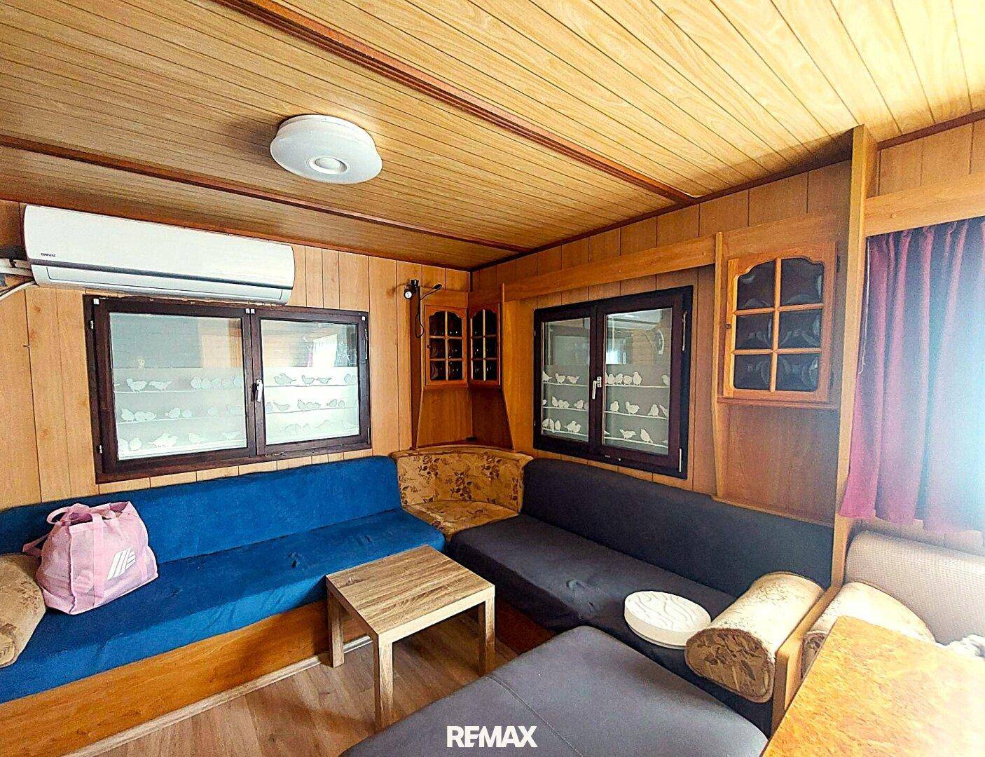 Wohnzimmer mit Holzwänden, Deckenverkleidung, Ecksofas und Klimaanlage.