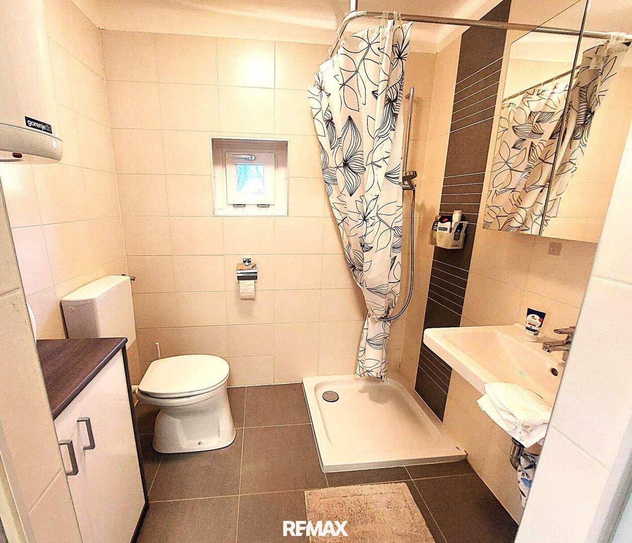 Gefliestes Badezimmer mit Dusche, Toilette und Waschbecken, funktional eingerichtet und mit Fenster.