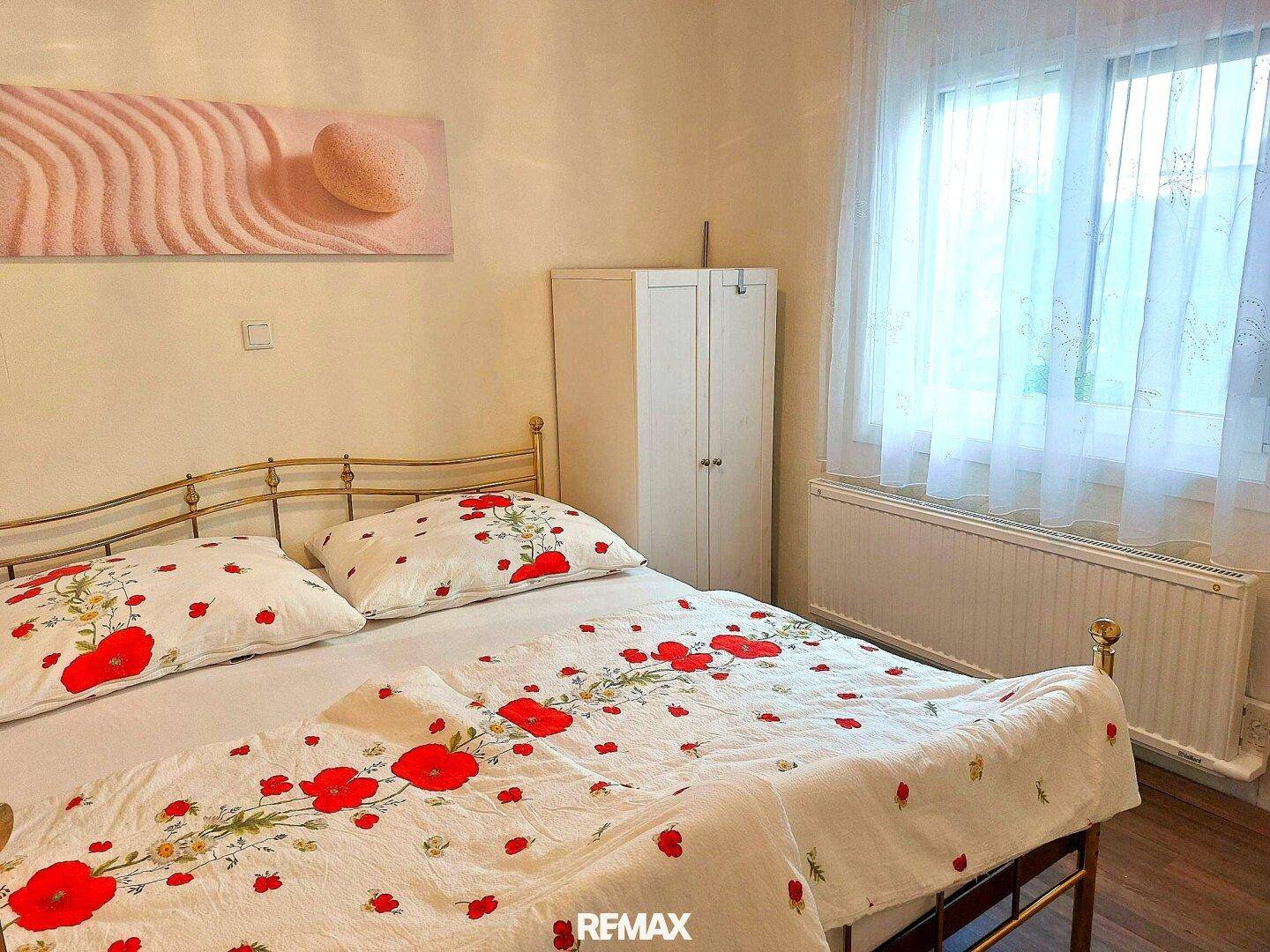 Schlafzimmer mit Doppelbett, floraler Bettwäsche und einem Fenster für natürliches Licht.