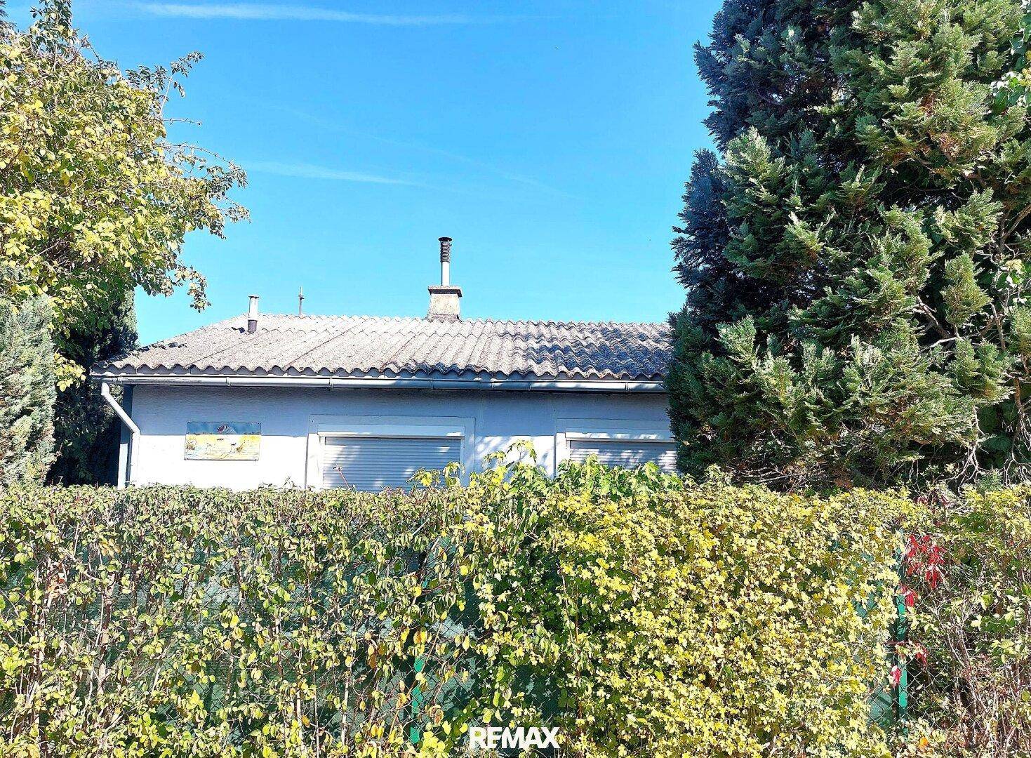 Rückansicht des Hauses mit Satteldach, umgeben von einer dichten grünen Hecke.