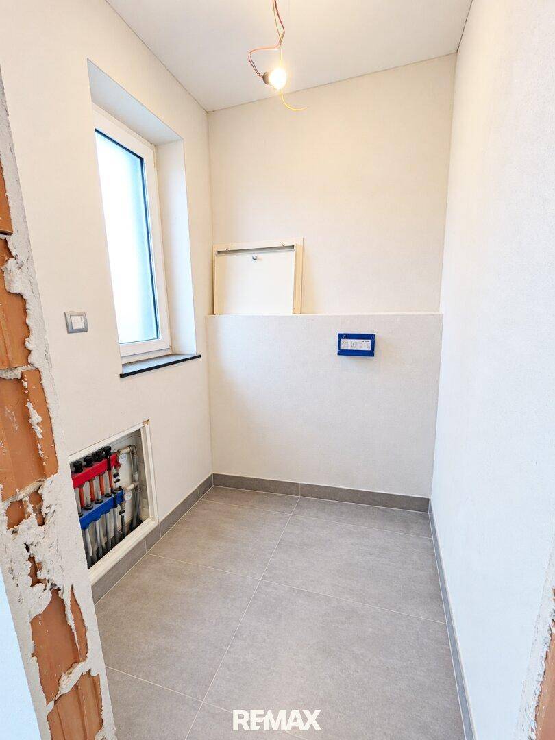 Kleiner Raum im Rohbau mit Fliesenboden und Fenster, vorbereitet für ein Gäste-WC.