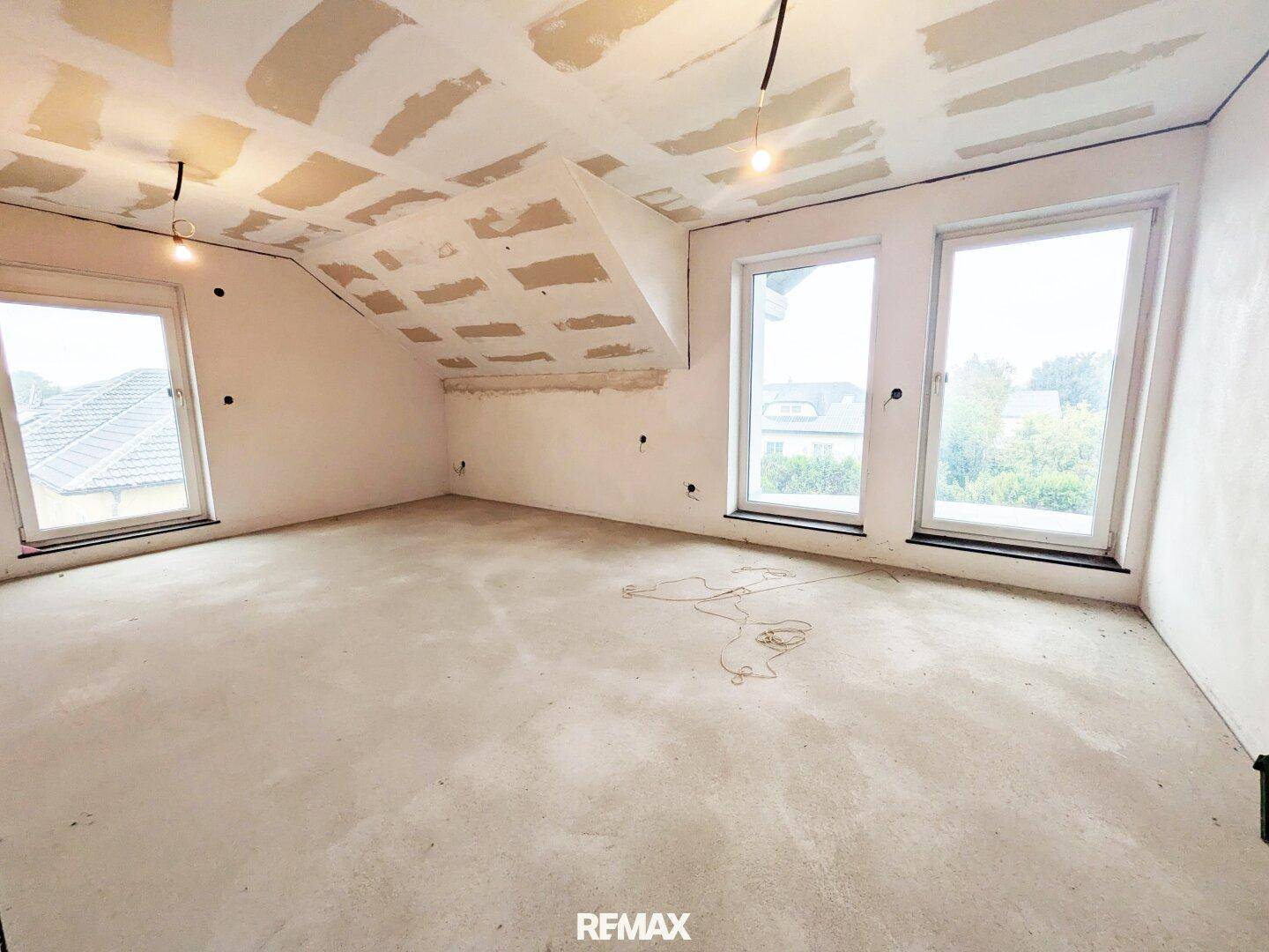 Helles Dachgeschosszimmer im Rohbau mit mehreren Fenstern und schrägen Decken.