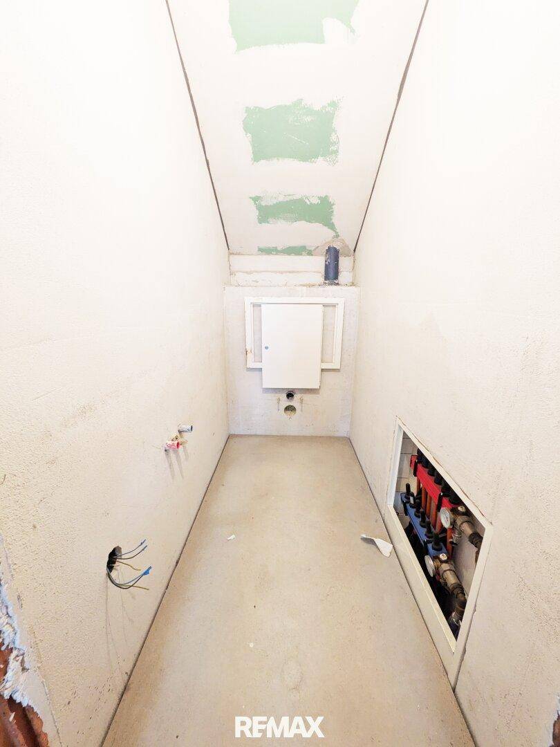 Schmaler Raum im Rohbau mit sichtbaren Installationen, ideal als Abstell- oder Technikraum.