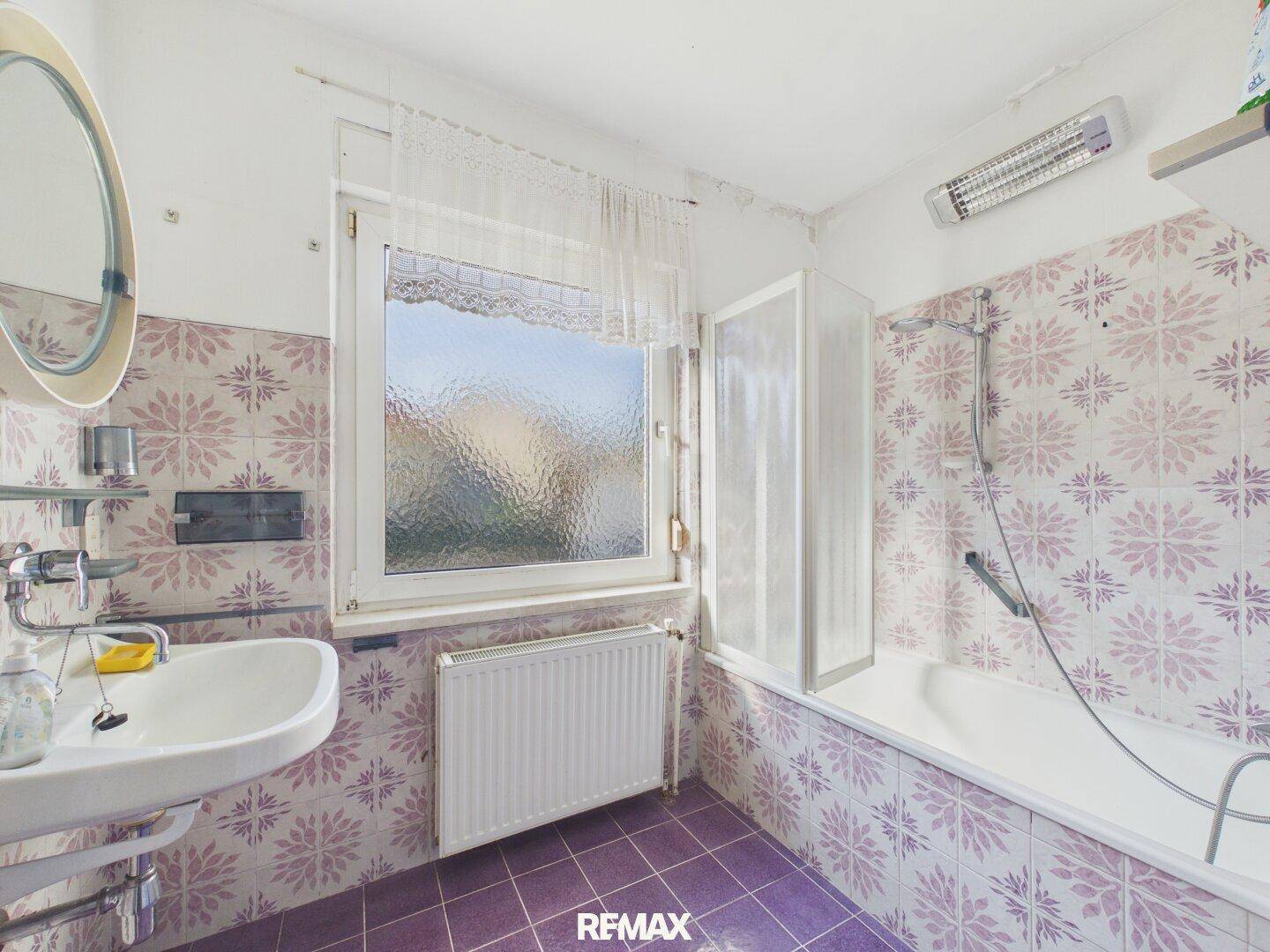 Badezimmer mit lila gemusterten Fliesen, Badewanne, Waschbecken und Fenster.