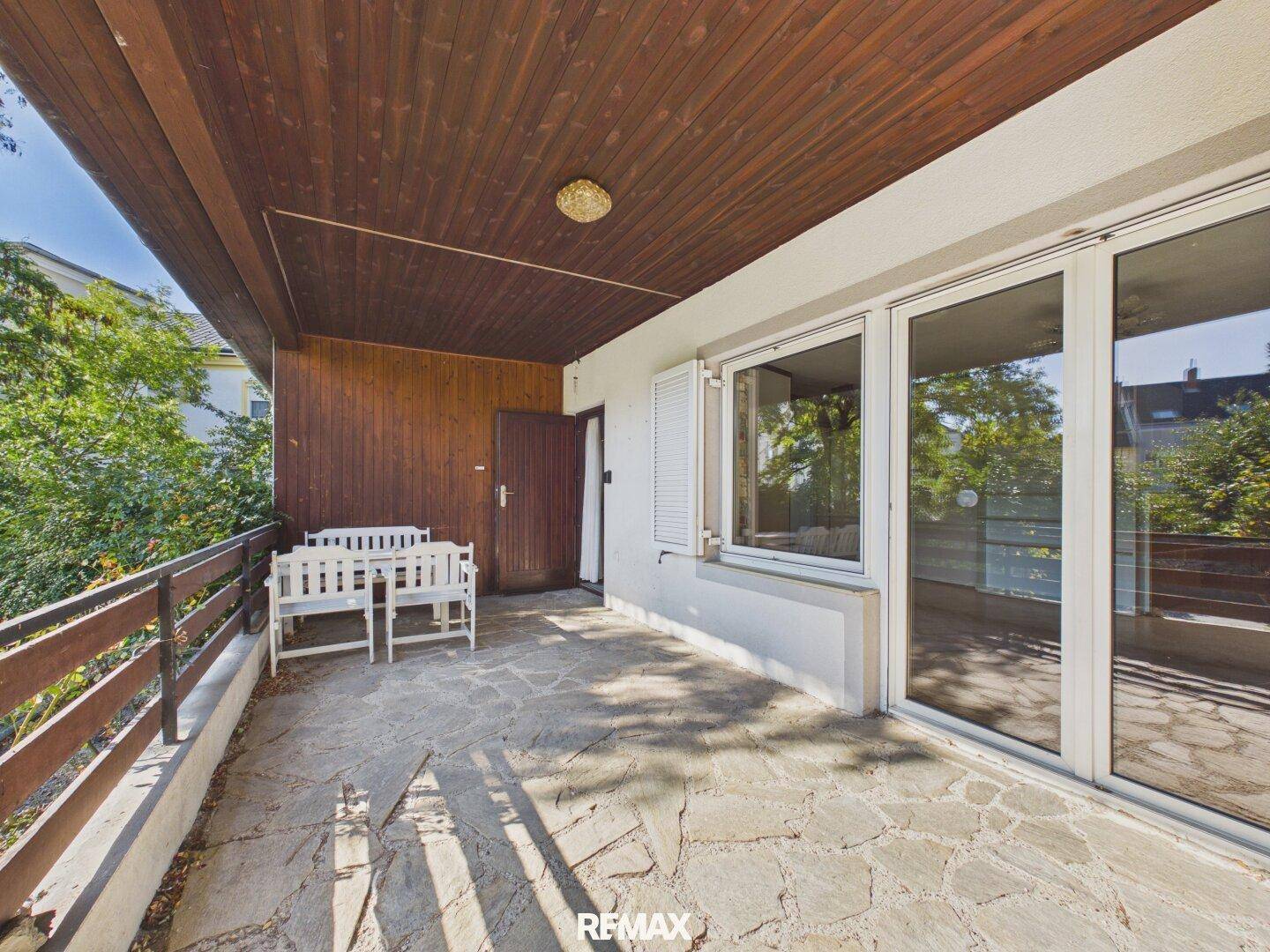 Überdachter Balkon mit Steinplattenboden, Holzbalkendecke und Gartenmöbeln.