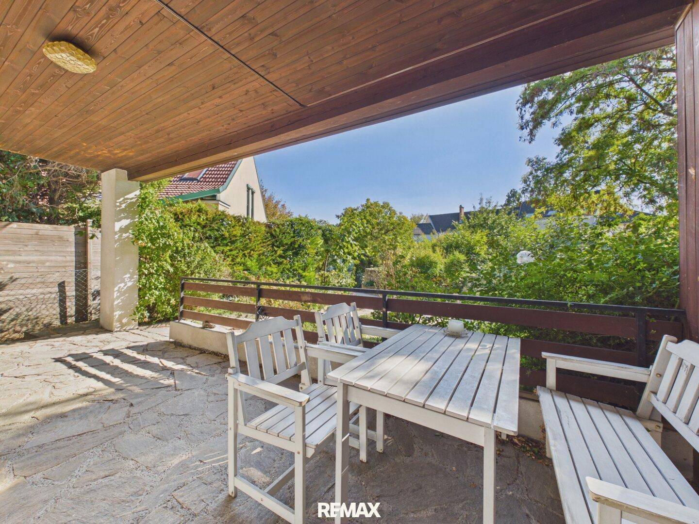 Gemütlicher Balkon mit Holztisch und Stühlen, umgeben von viel Grün und Bäumen.