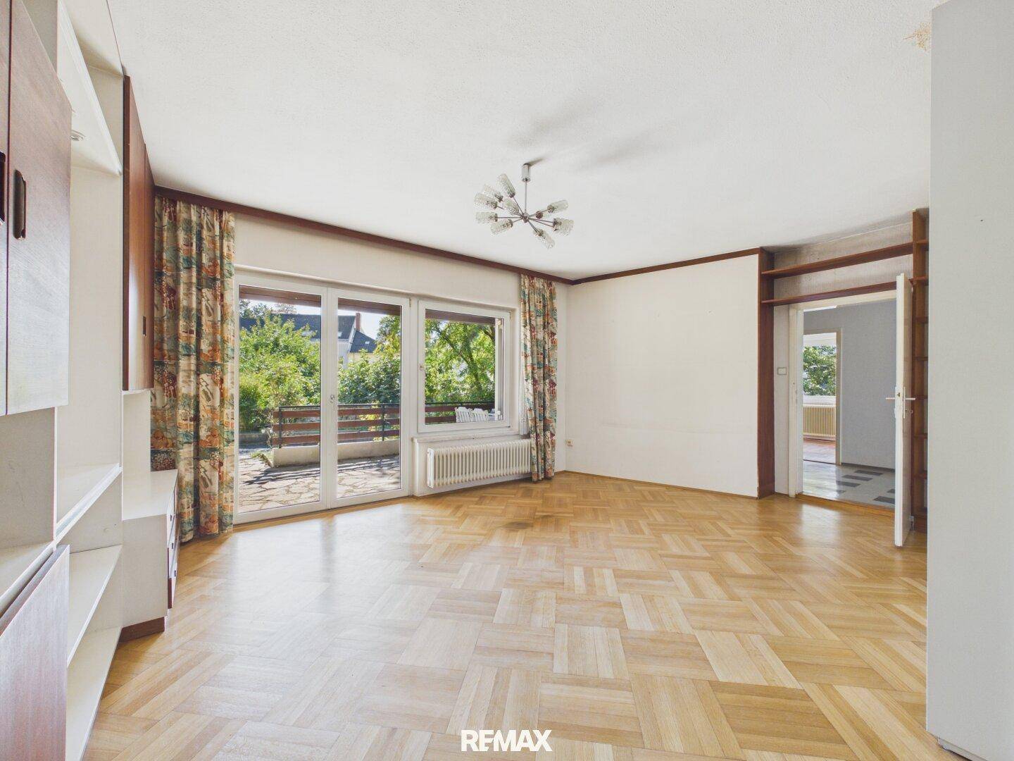 Helles Wohnzimmer mit Parkettboden, großen Fenstern und Zugang zu einem Balkon.