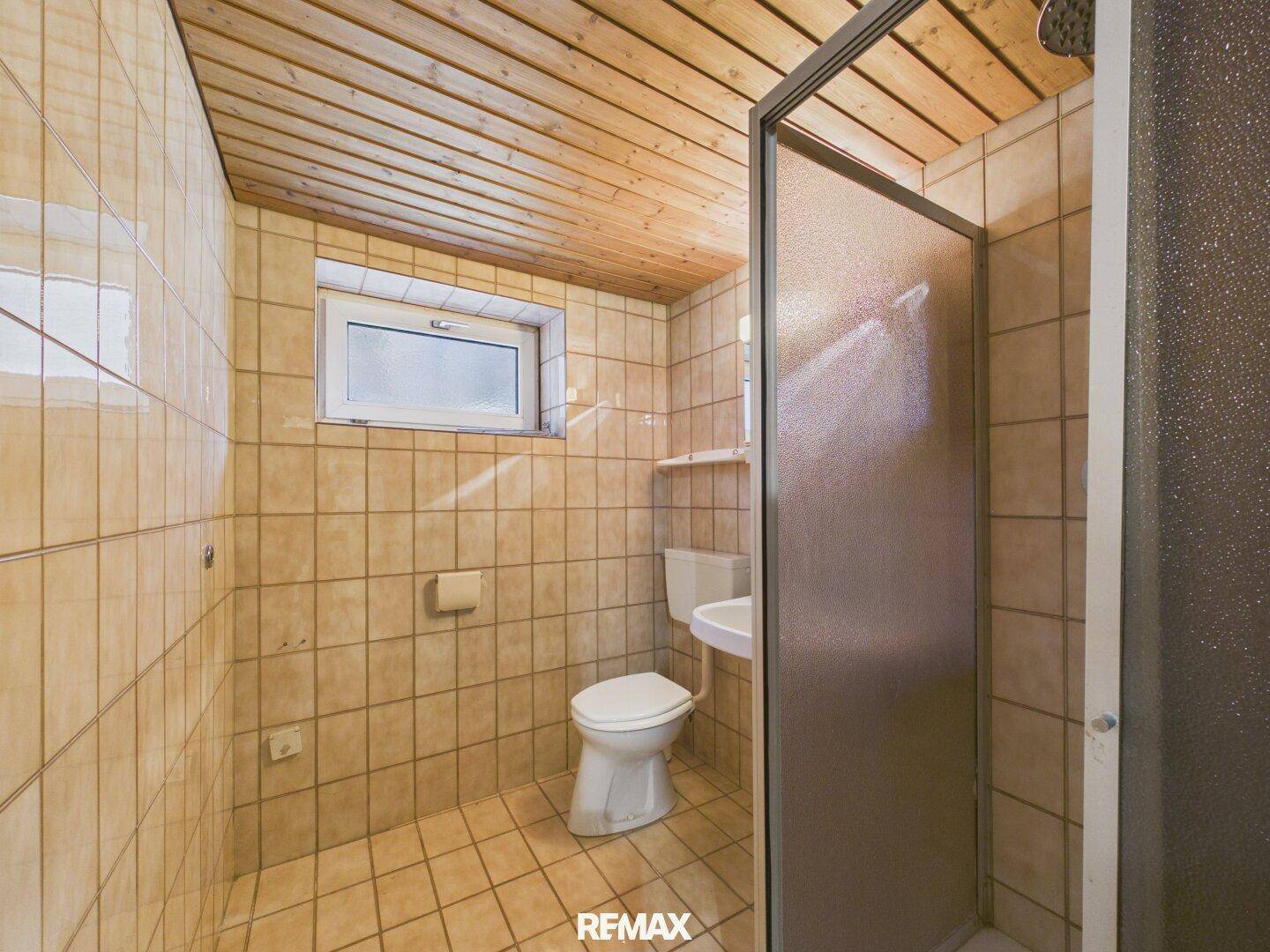 Einfaches Badezimmer im Keller mit Dusche, WC, Waschbecken und Holzdecke.
