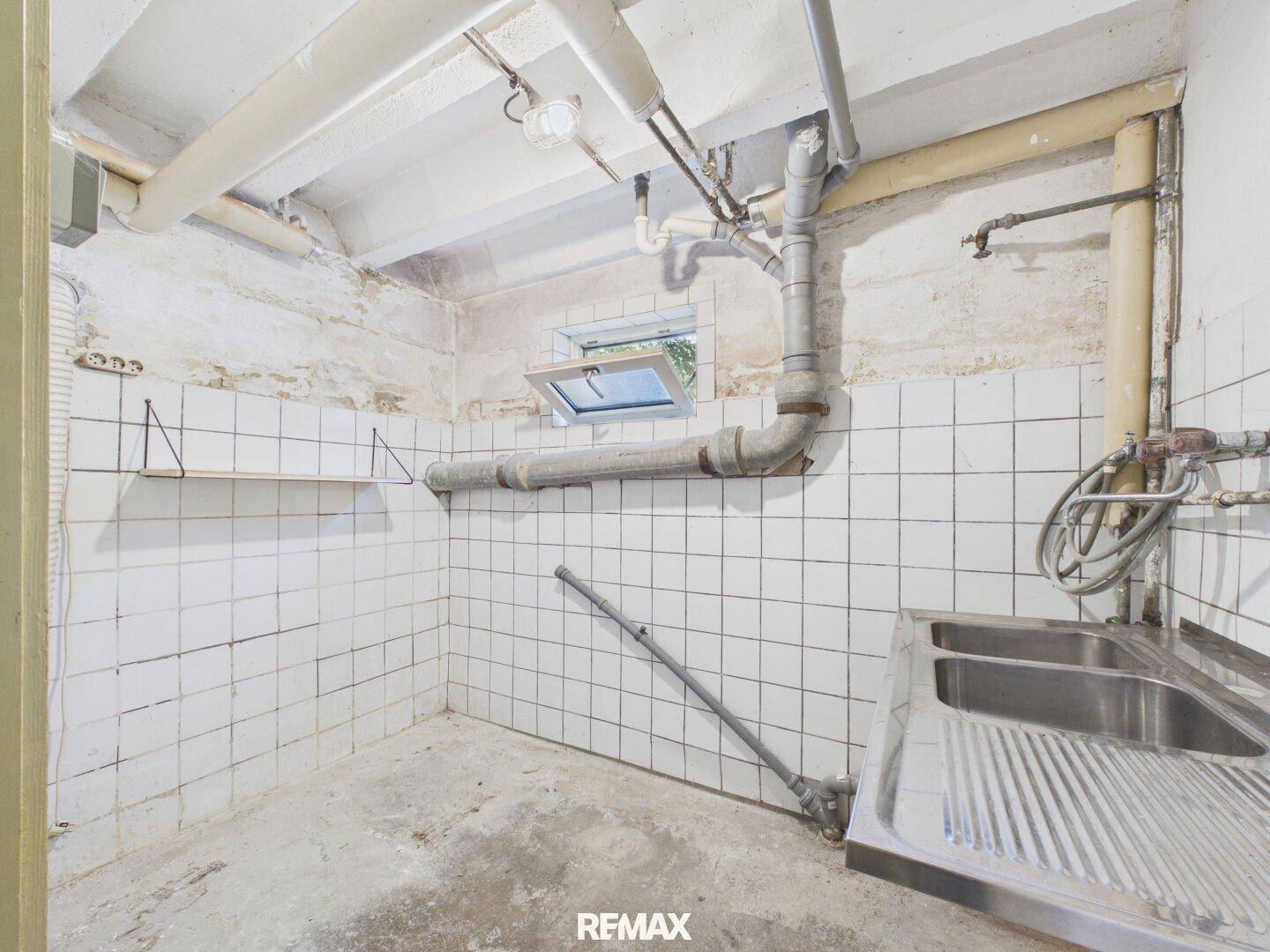 Waschküche im Keller mit Waschbecken, Fliesenwänden und freiliegenden Rohren.