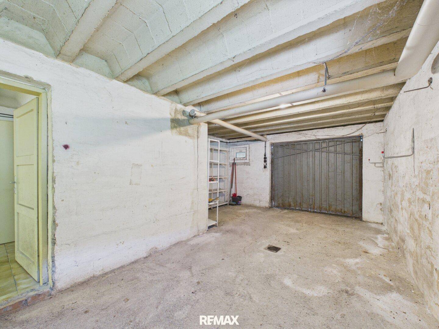 Geräumige Garage im Untergeschoss mit Betonboden und Metalltor.