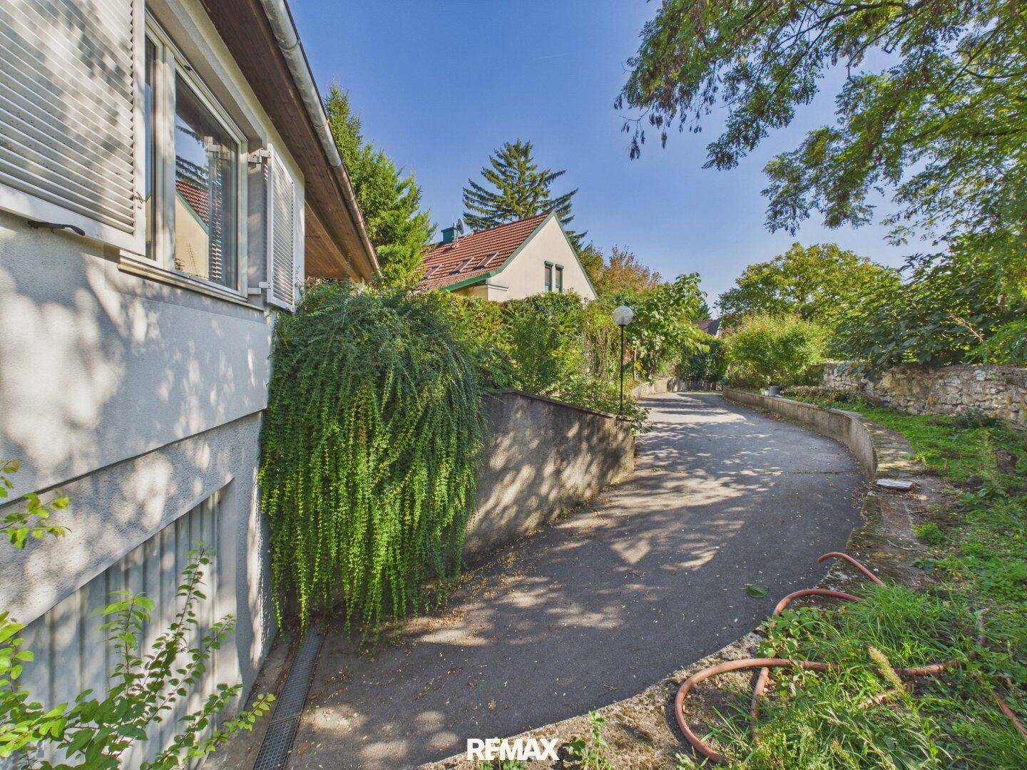 Seitenansicht des Hauses mit Zufahrt und üppiger Bepflanzung entlang der Mauer.
