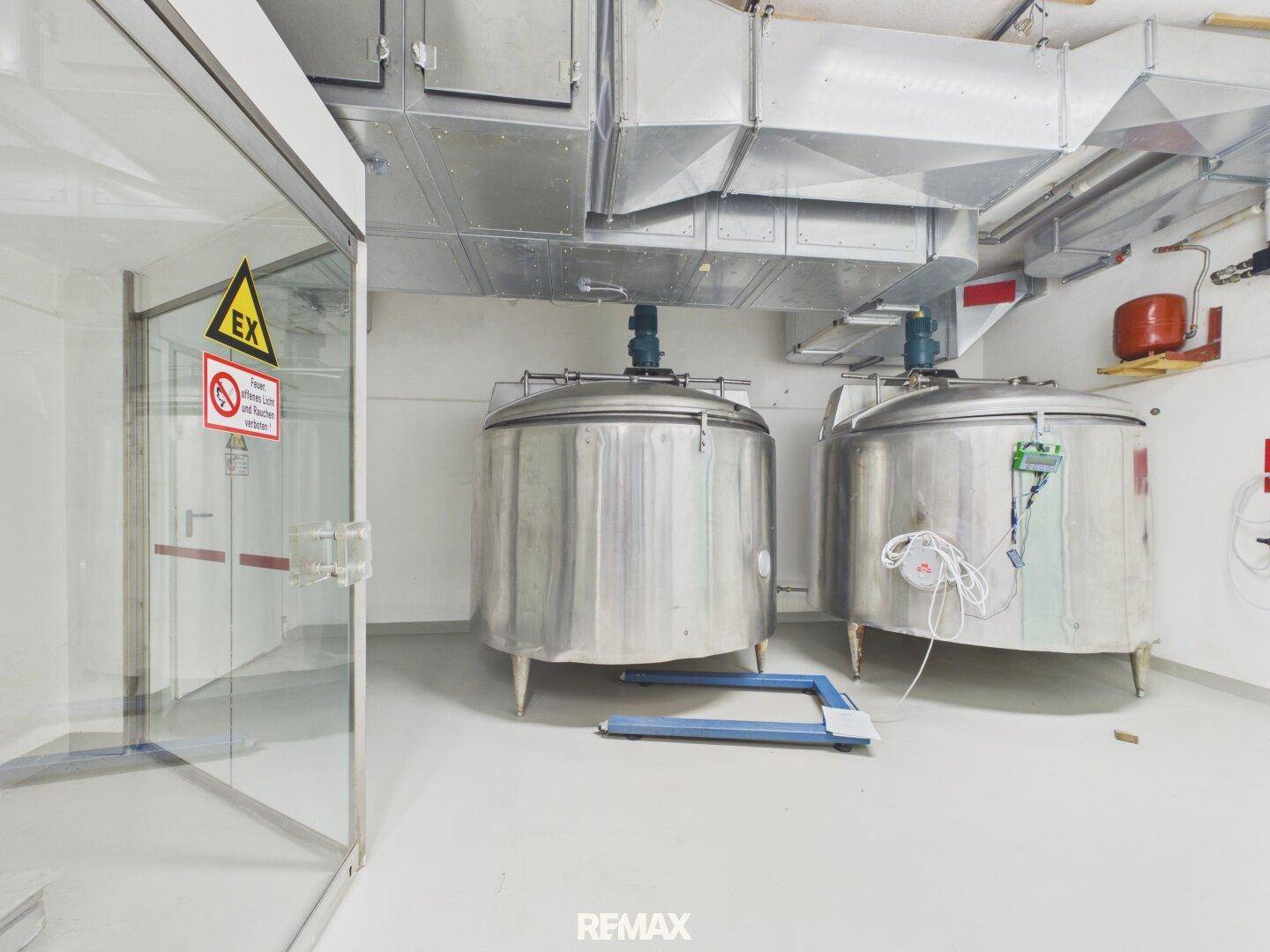 Raum mit großen Edelstahltanks, möglicherweise zur Lagerung oder Verarbeitung, und sichtbaren Lüftungskanälen.