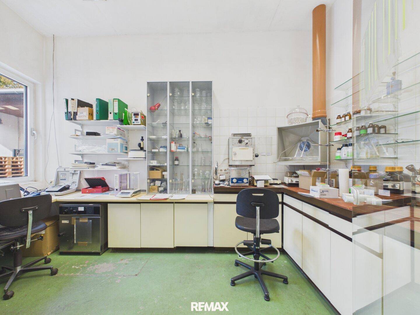 Laborraum mit wissenschaftlicher Ausrüstung, Glaswaren, Regalen und einem grünen Bodenbelag.