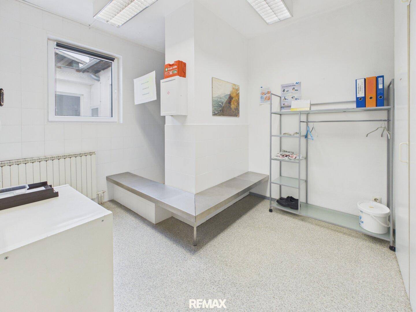 Umkleideraum oder Pausenbereich mit einer langen Sitzbank, einem Fenster und einem Kleiderständer.