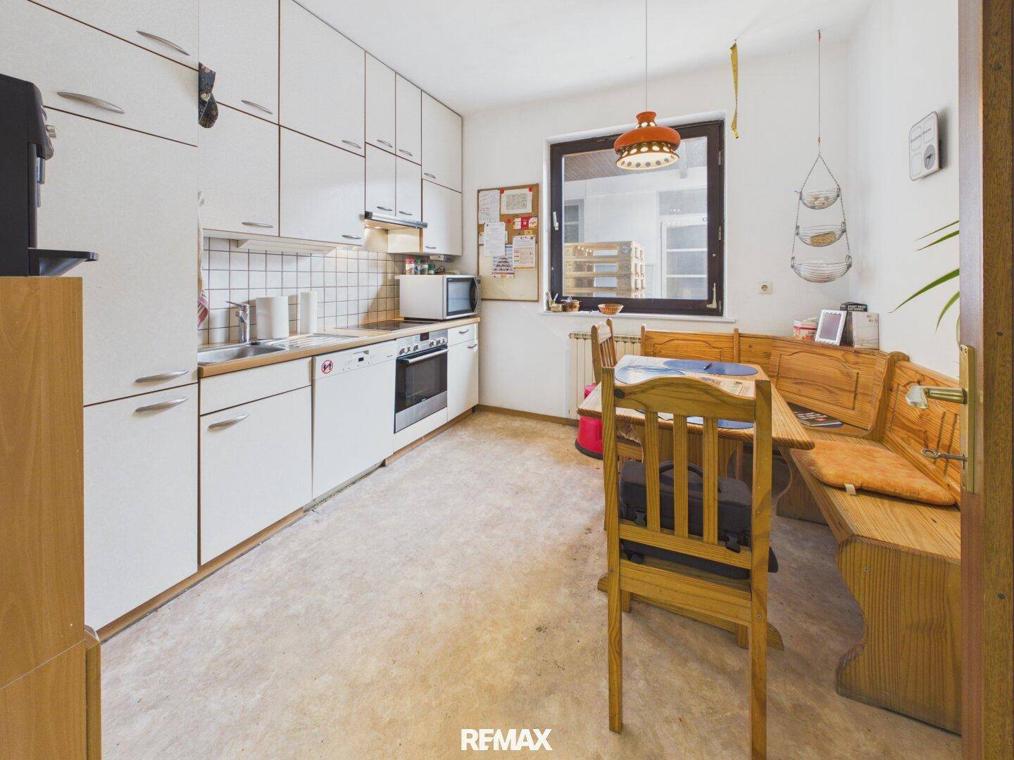 Traditionelle Küche mit weißen Schränken, einer Essecke und einem Fenster, das Tageslicht hereinlässt.