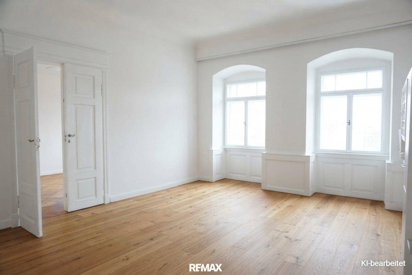 Renoviertes Zimmer mit weiß gestrichenen Wänden, Holzboden und großen Bogenfenstern, hell und modern.