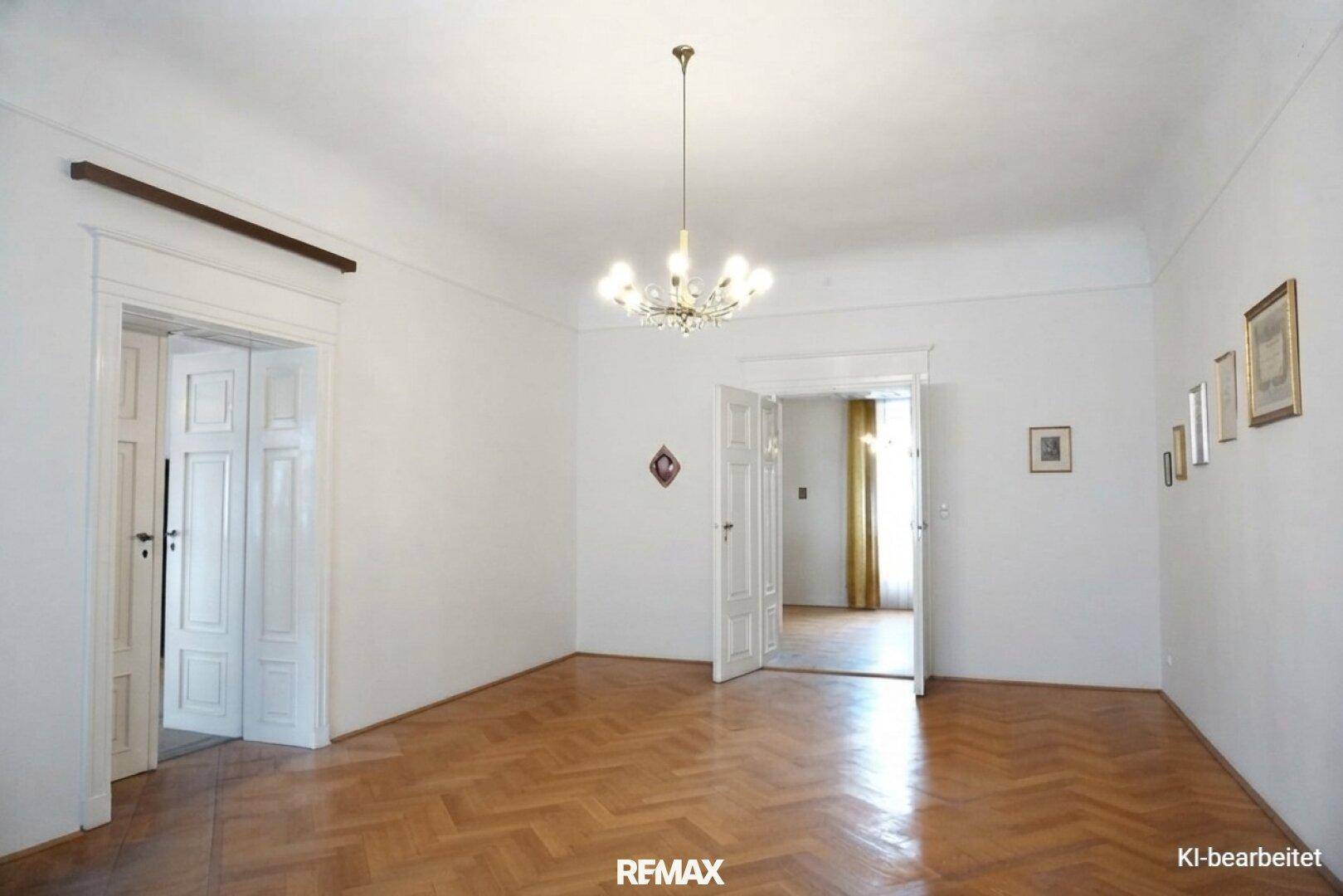 Renoviertes Zimmer mit weißen Wänden, Fischgrätparkett und einem eleganten Kronleuchter, hell und einladend.