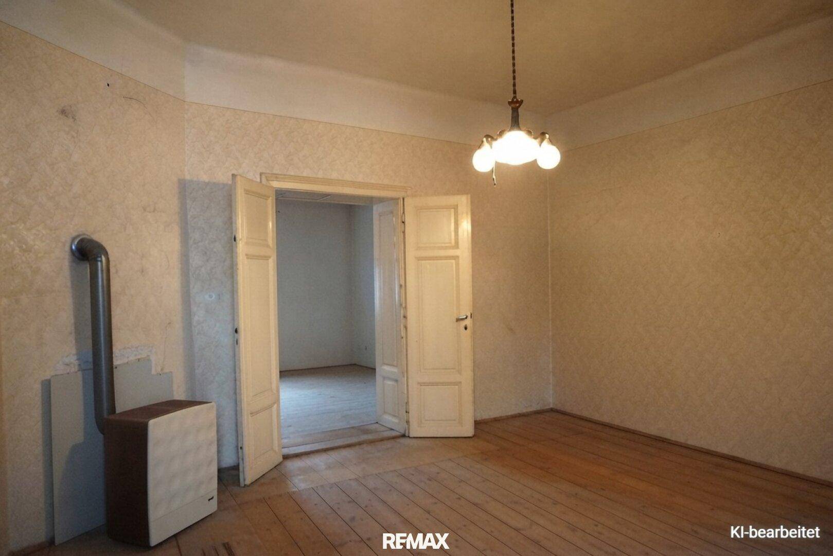 Zimmer mit gemusterter Tapete, Holzdielenboden und einem Ofen, der auf eine Renovierung wartet.