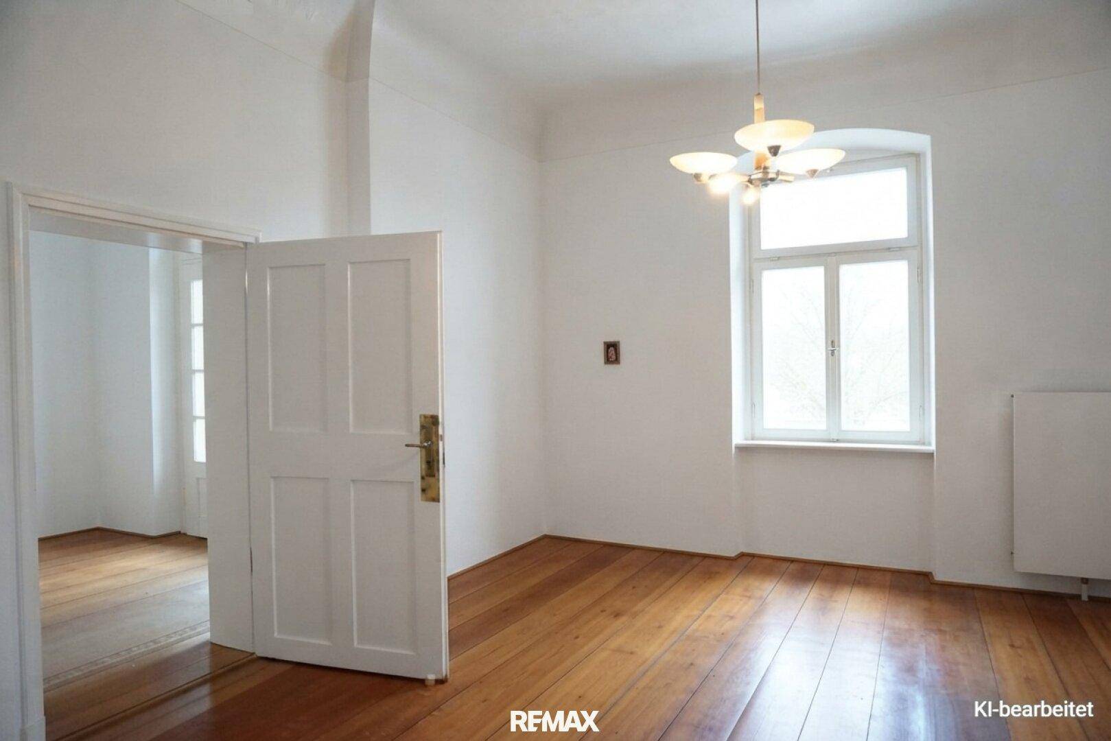 Renoviertes Zimmer mit weißen Wänden, Holzdielenboden und einem hohen Fenster, hell und einladend.