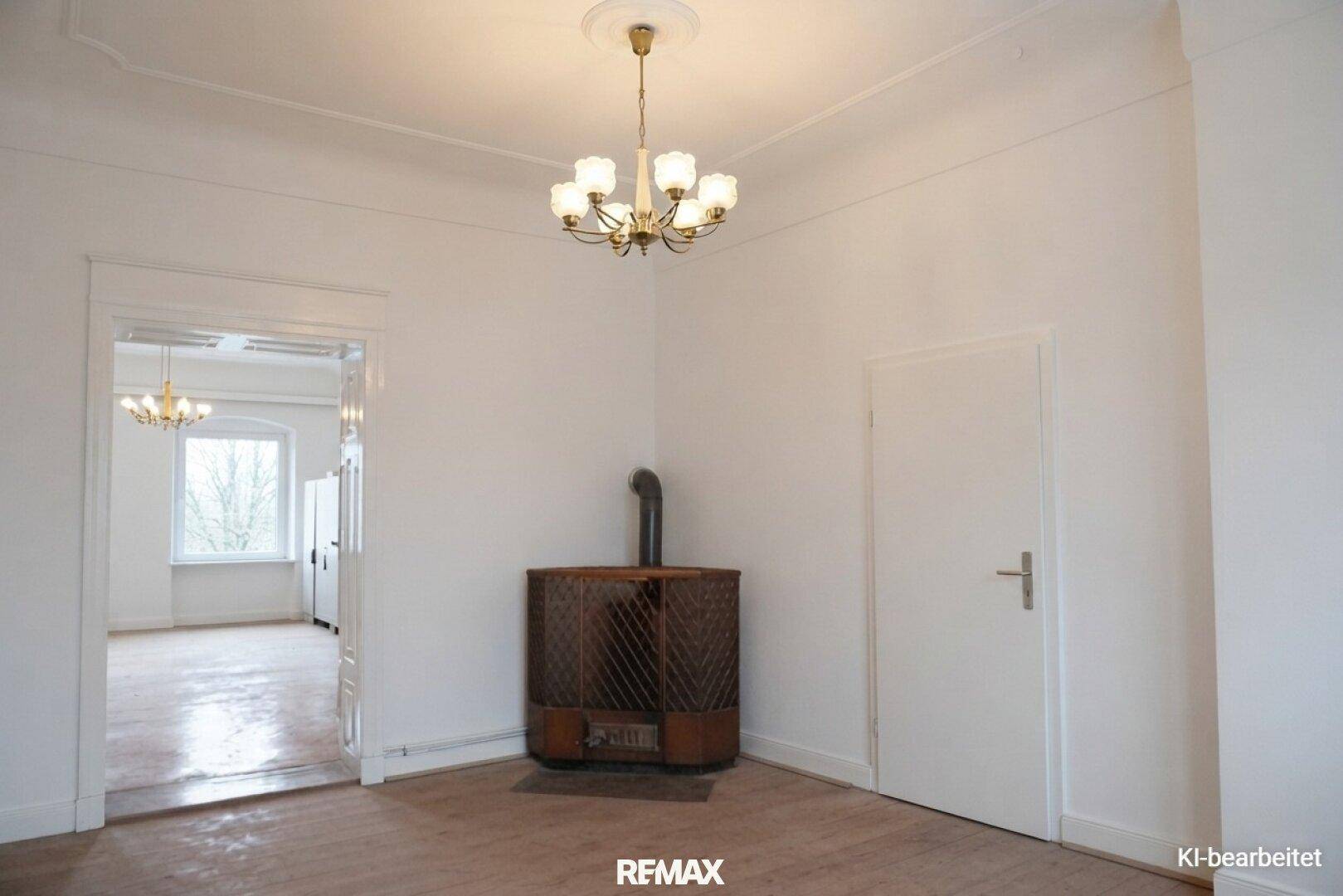 Renoviertes Zimmer mit weißen Wänden, Holzdielenboden und einem Ofen, der modernisiert wurde.