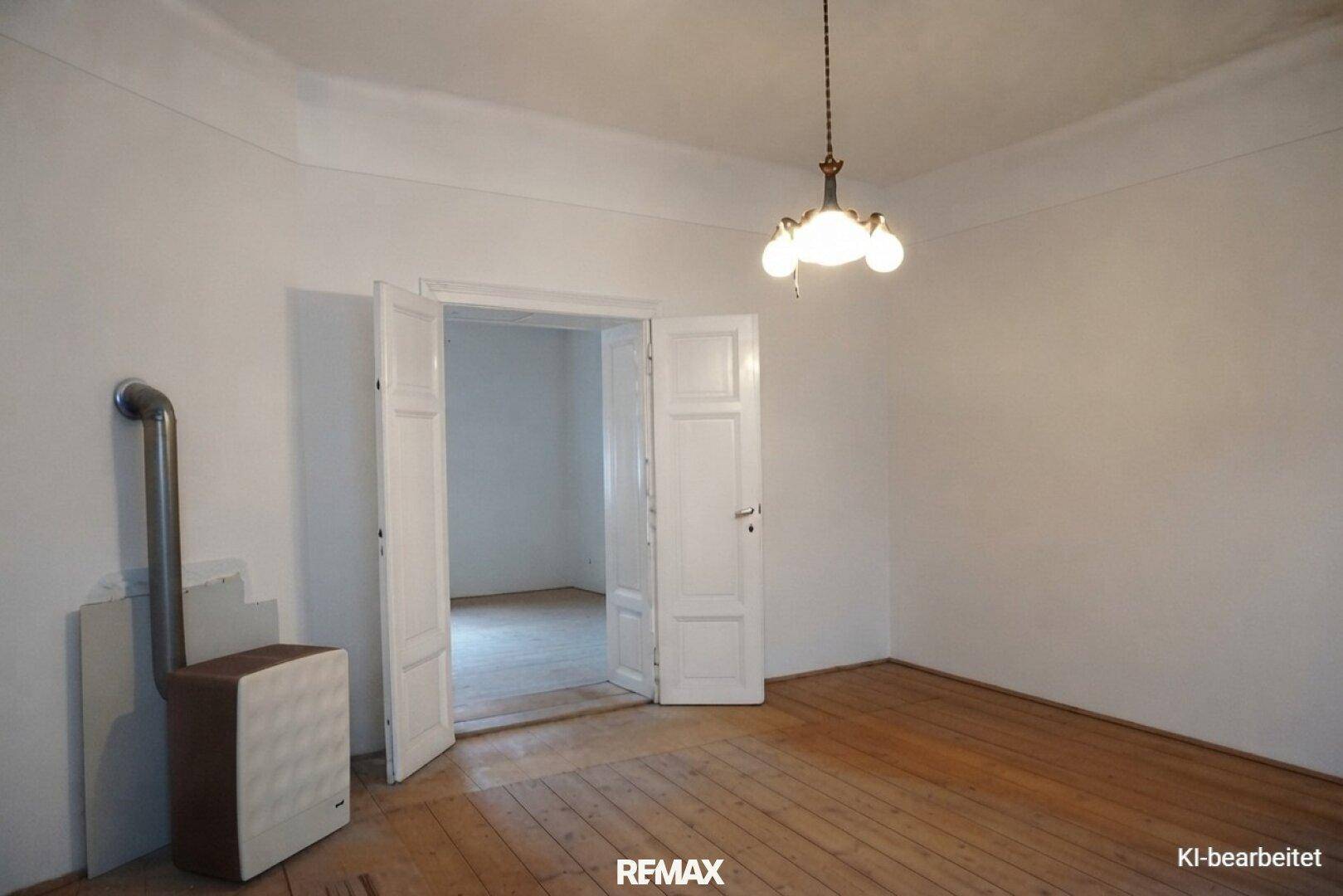 Renoviertes Zimmer mit weißen Wänden, Holzdielenboden und einem Ofen, der modernisiert wurde.