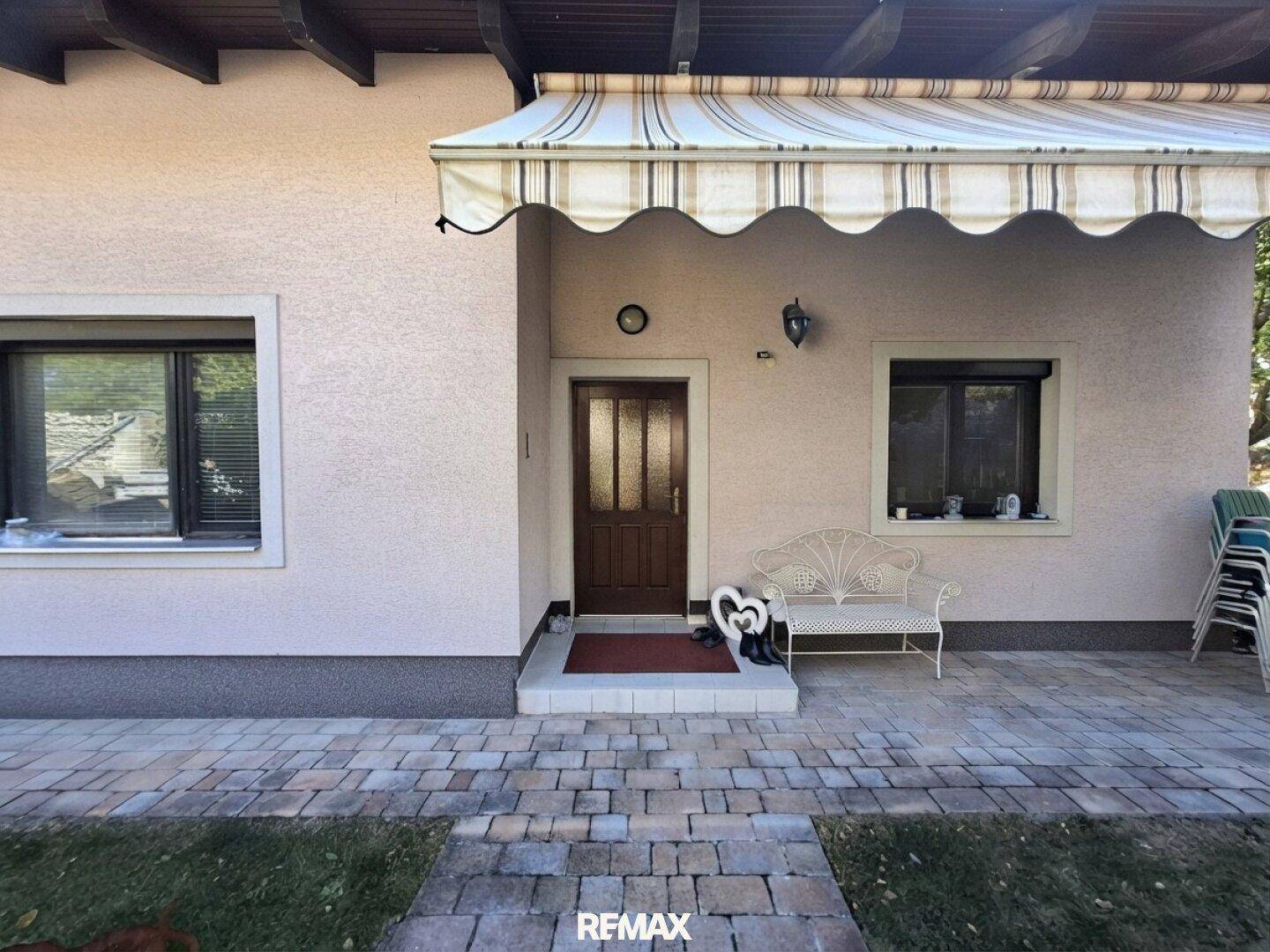 Eingangsbereich des Hauses mit Vordach, Sitzbank und gepflastertem Weg.