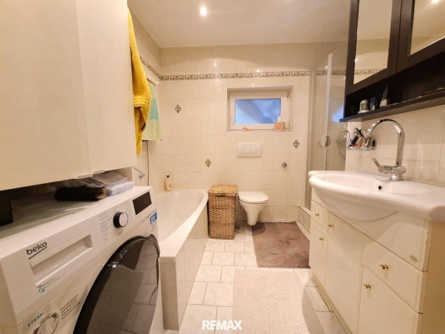Gefliestes Badezimmer mit Badewanne, Dusche, Waschbecken und Fenster.