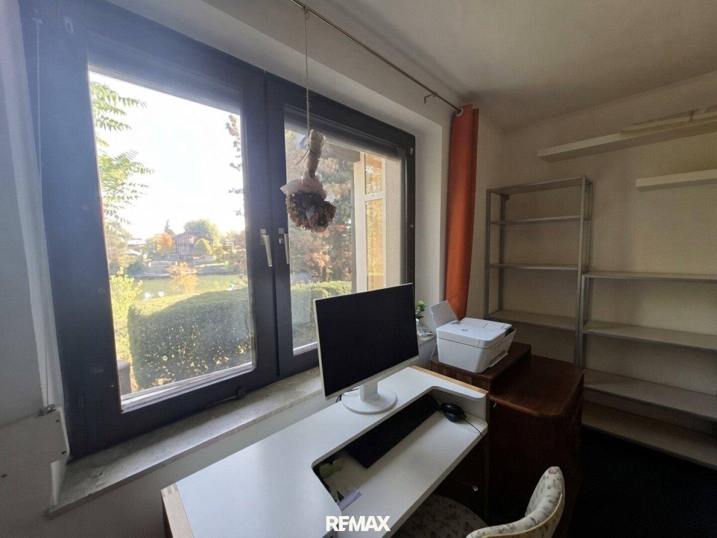 Arbeitszimmer mit Schreibtisch, Regal und großem Fenster mit Seeblick.