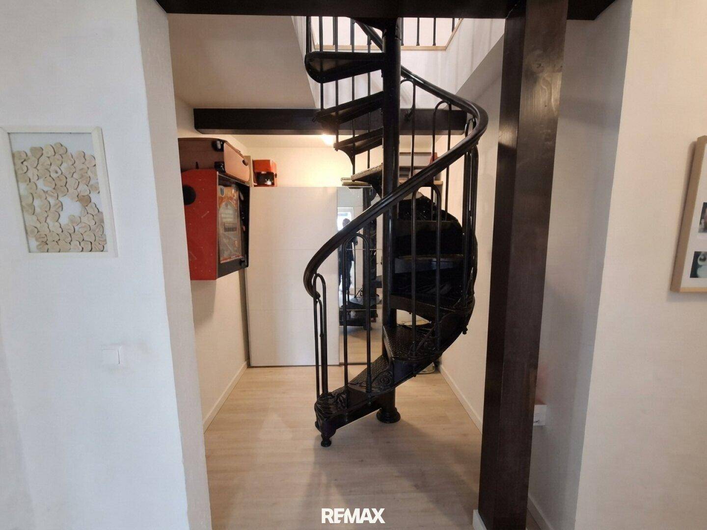 Flur mit einer eleganten schwarzen Wendeltreppe und hellem Boden.