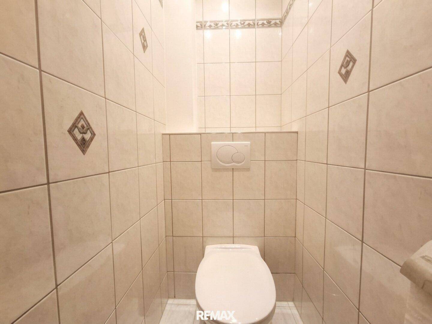 Kleines Gäste-WC mit beigefarbenen Fliesen und wandhängendem WC.
