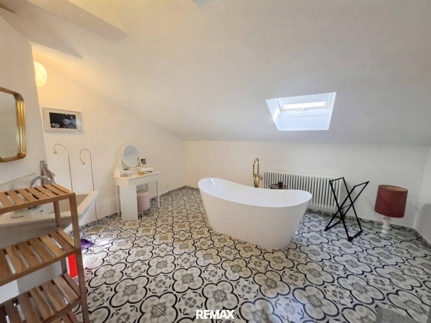 Großes Badezimmer im Dachgeschoss mit freistehender Badewanne, Oberlicht und gemusterten Fliesen.