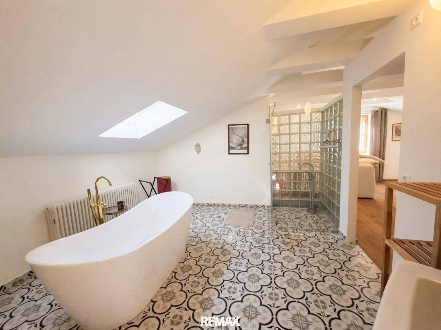 Geräumiges Dachgeschossbad mit freistehender Wanne, Glasbausteinwand und gemustertem Fliesenboden.