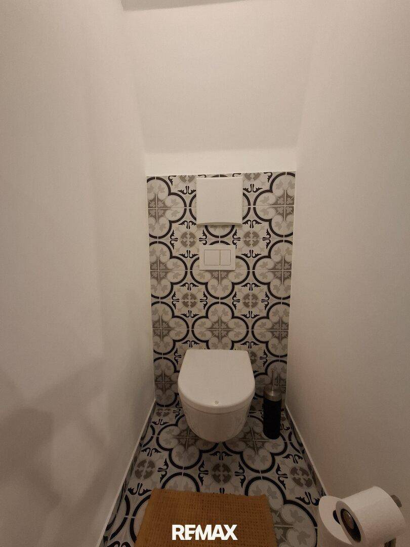 Modernes Gäste-WC mit gemusterten Fliesen an Wand und Boden.