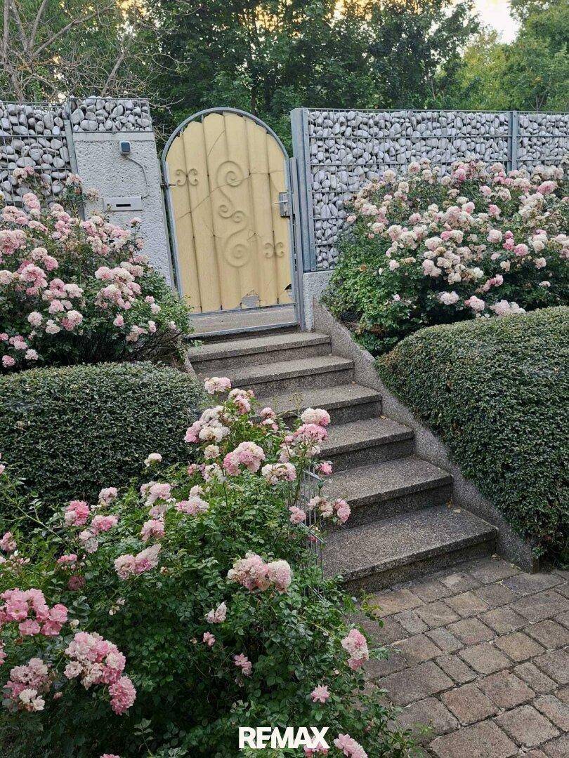Gartenweg mit Steintreppe, Rosenbüschen und einem dekorativen Gartentor.