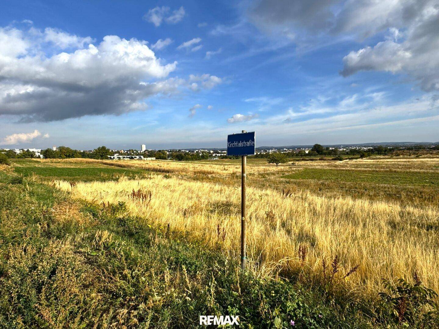 Blick über weite Felder mit einem Straßenschild und Häusern am Horizont.