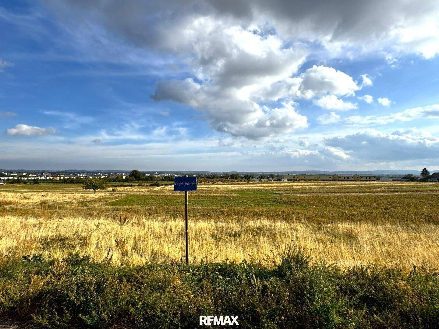 Panoramablick auf grüne Felder und das Straßenschild Kirchtalstraße unter blauem Himmel.