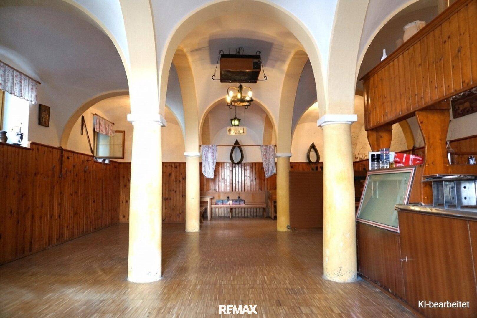 Weitläufiger Saal mit mehreren Bögen, Säulen und einer Theke, ideal für größere Zusammenkünfte.
