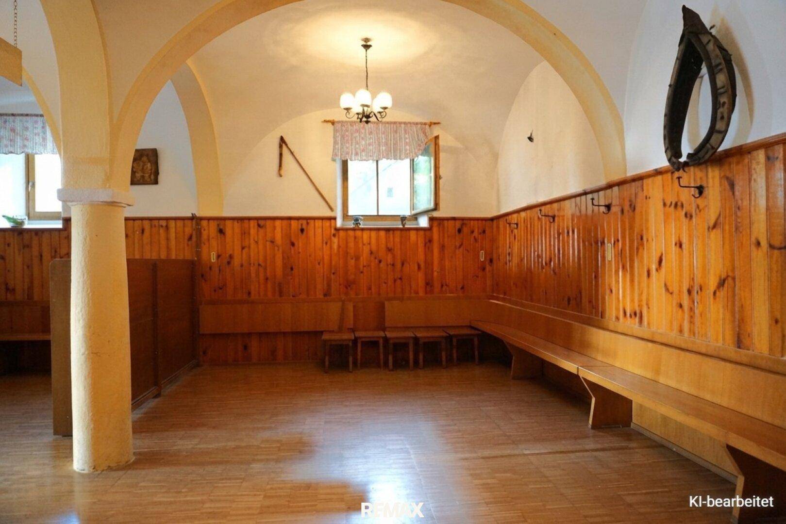 Traditioneller Saal mit gewölbten Decken, Holzbänken und einem Kronleuchter, der eine gemütliche Atmosphäre schafft.