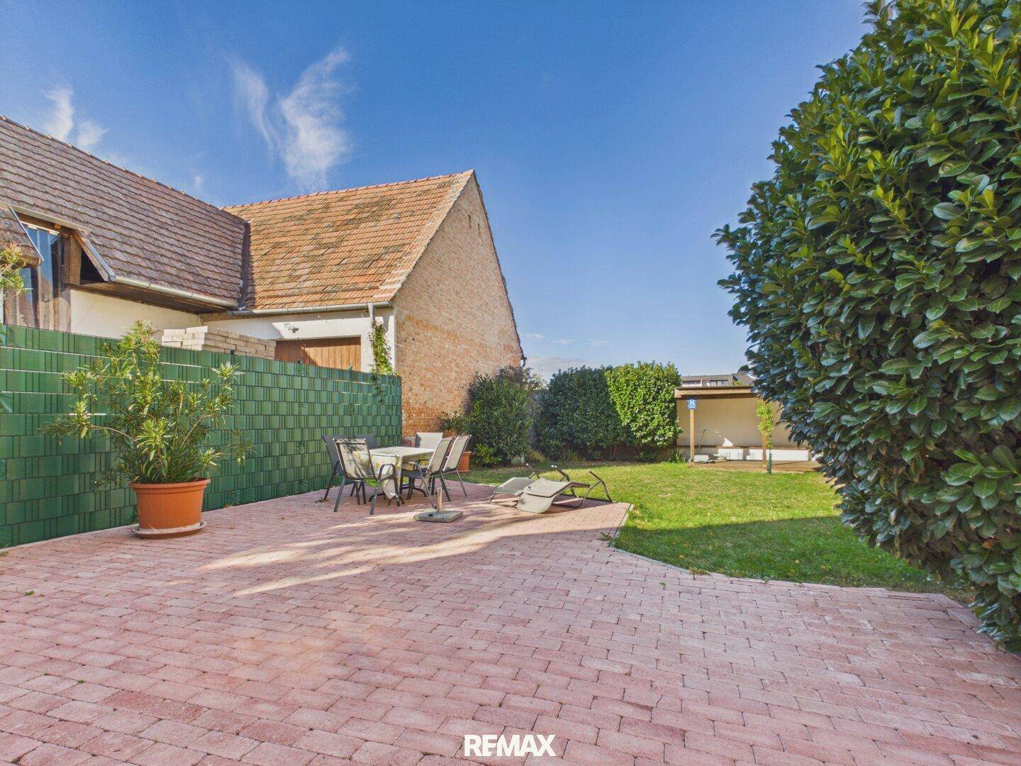 Sonniger Gartenbereich mit gepflasterter Terrasse, Rasenfläche und Gartenmöbeln für entspannte Stunden.
