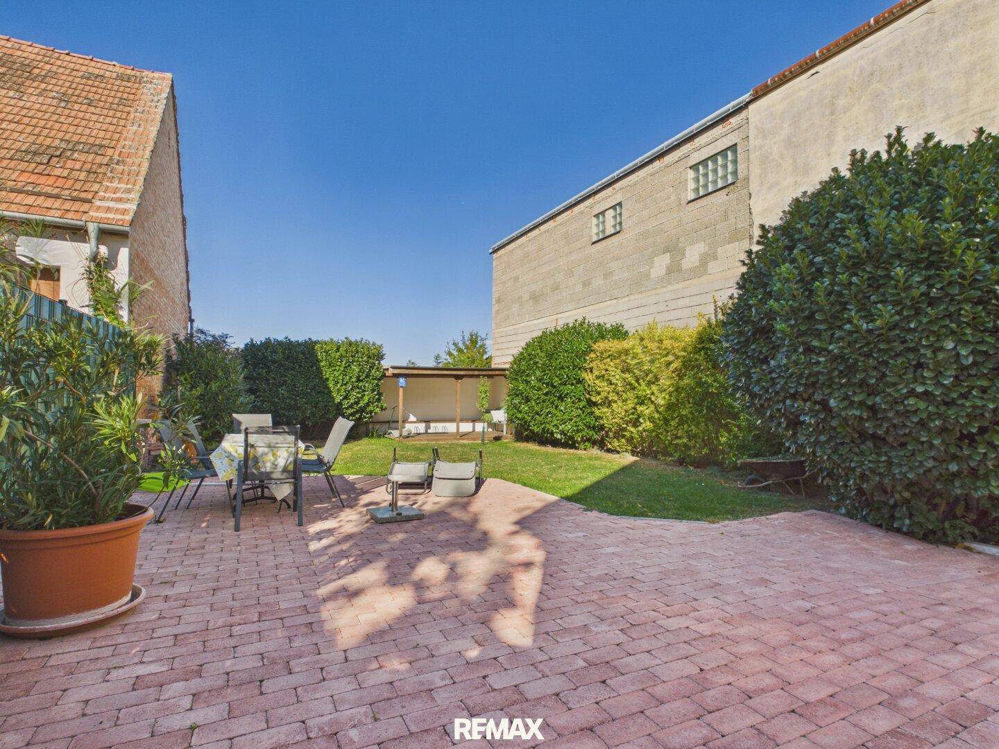 Weitläufiger Garten mit großer gepflasterter Terrasse und gepflegter Rasenfläche zwischen den Gebäuden.