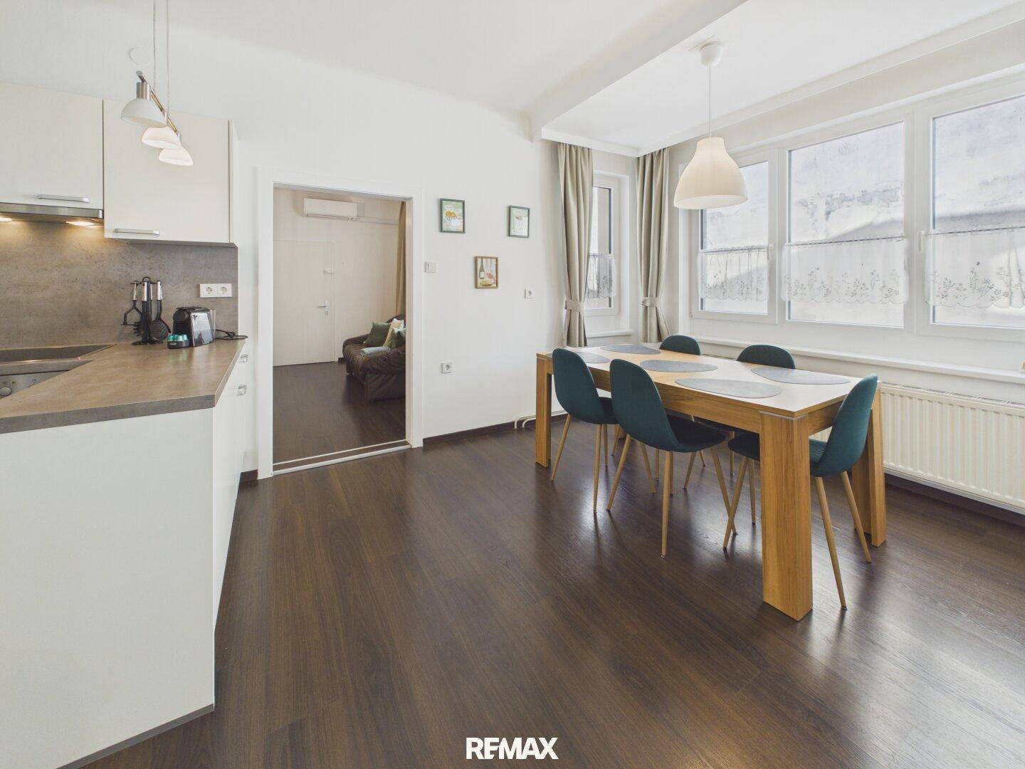 Offener Wohn- und Essbereich mit moderner Küche, Esstisch und Zugang zu einem weiteren Zimmer.