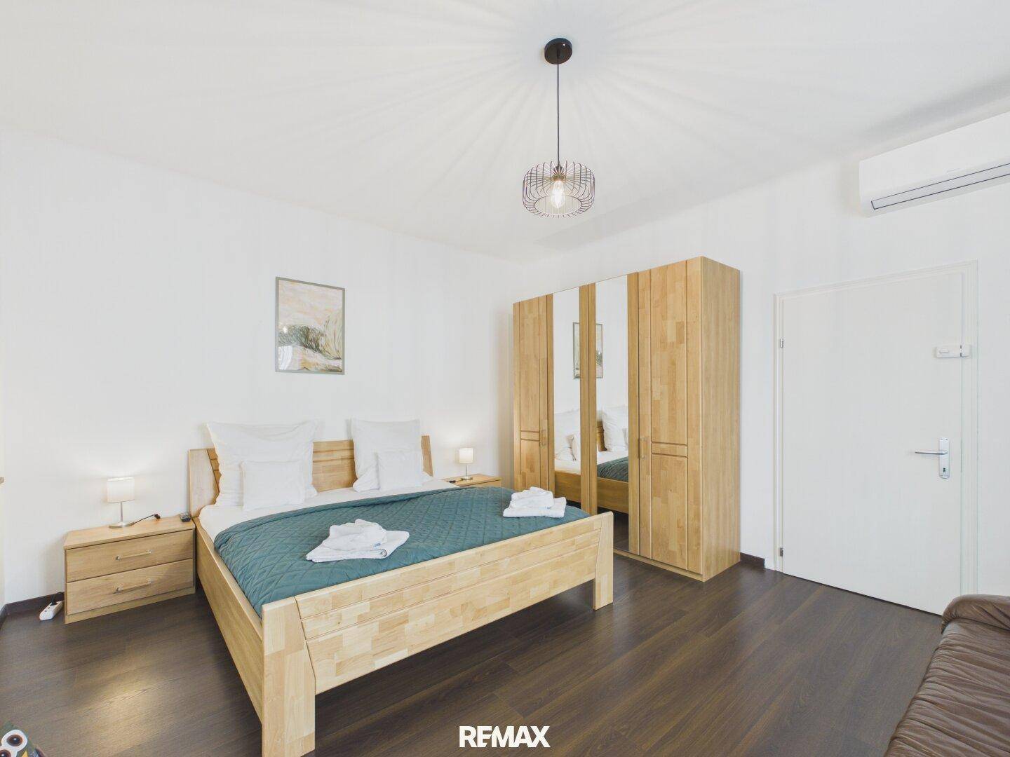 Schlafzimmer mit Holzbett, Spiegelschrank und Klimaanlage für angenehme Raumtemperatur.