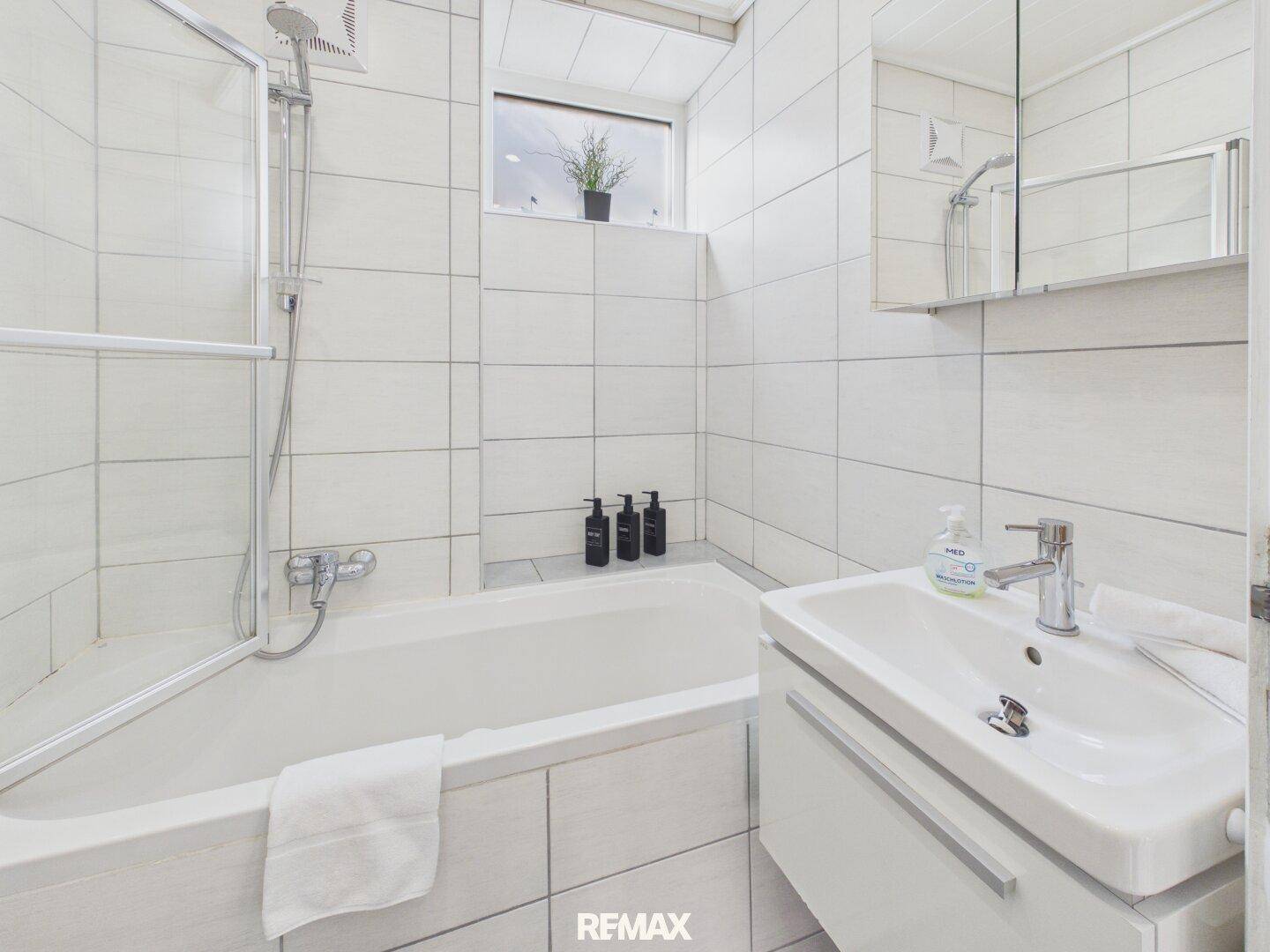 Helles Badezimmer mit Badewanne, Duschfunktion, Waschbecken und Fenster für natürliche Belüftung.