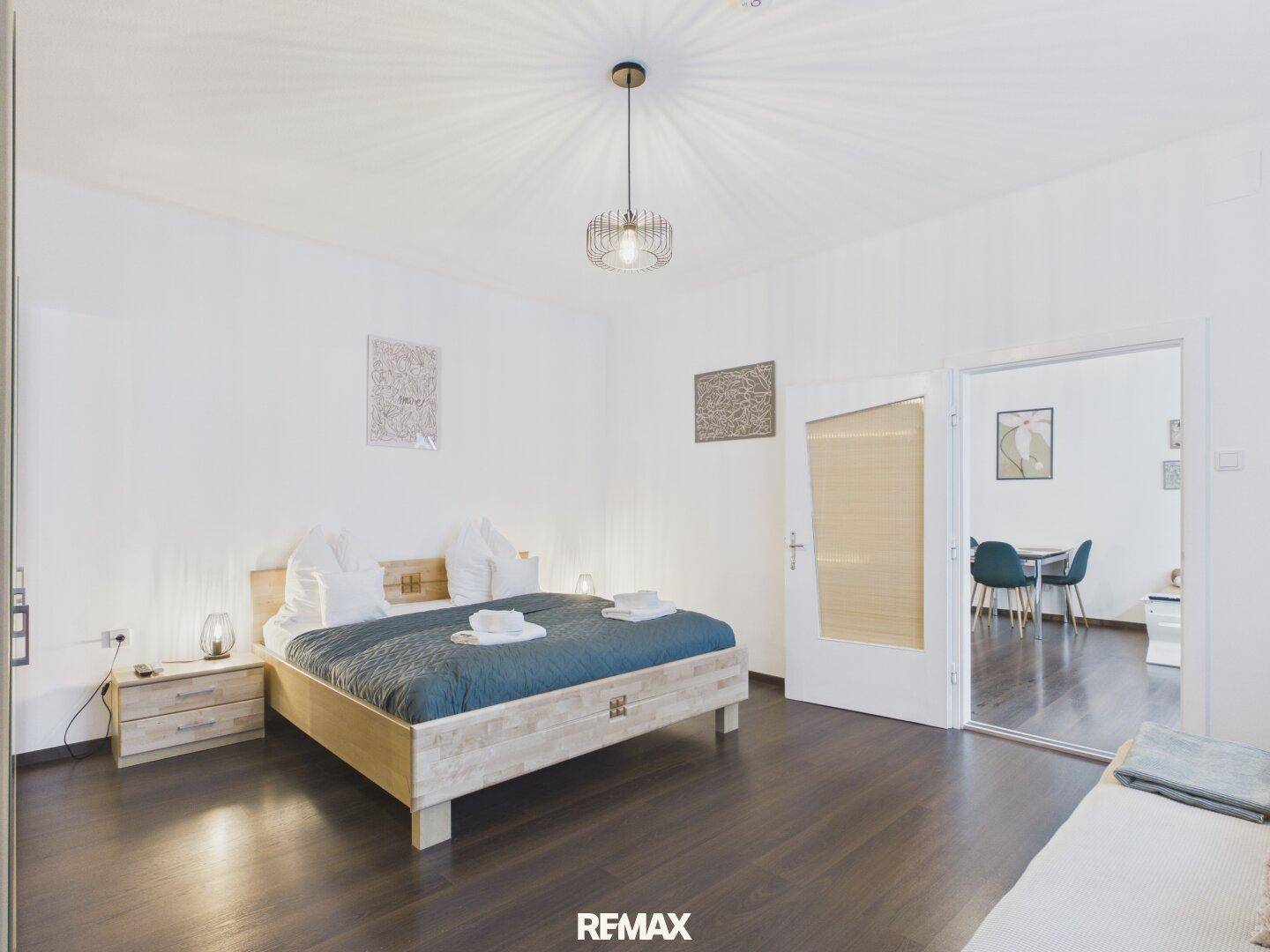 Schlafzimmer mit Holzbett und Blick durch die offene Tür in den angrenzenden Wohnbereich.