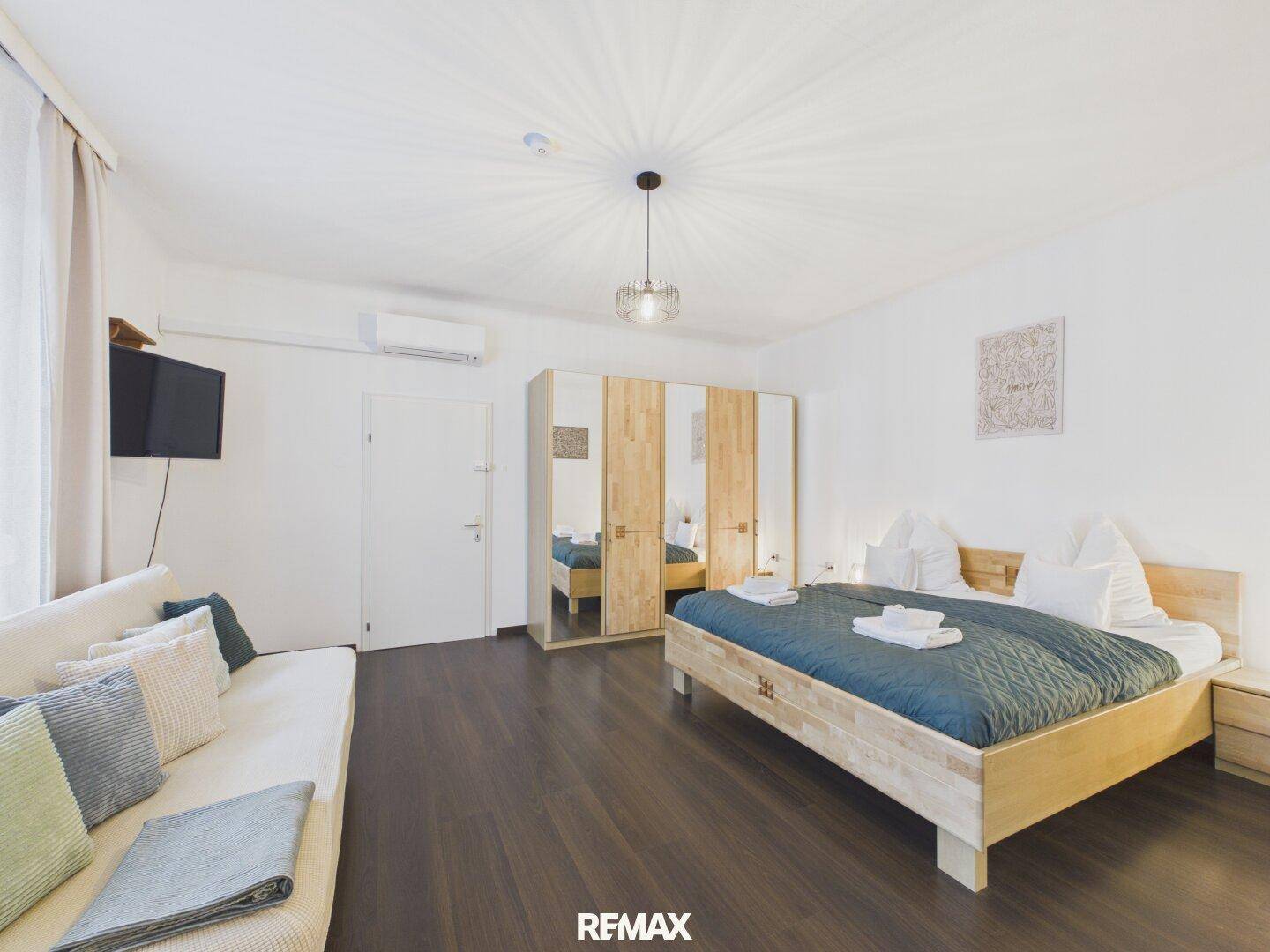 Geräumiges Schlafzimmer mit Holzbett, Sofa und großem Spiegelschrank für viel Stauraum.