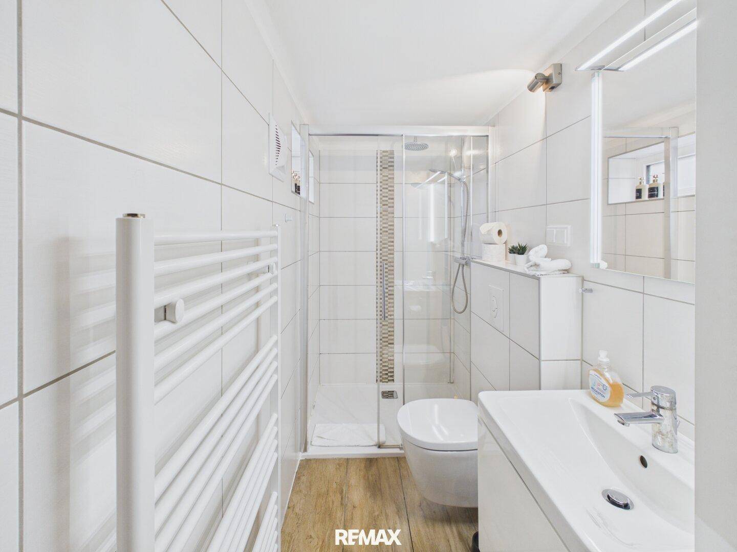 Modernes Badezimmer mit ebenerdiger Dusche, WC, Waschbecken und beheiztem Handtuchhalter.