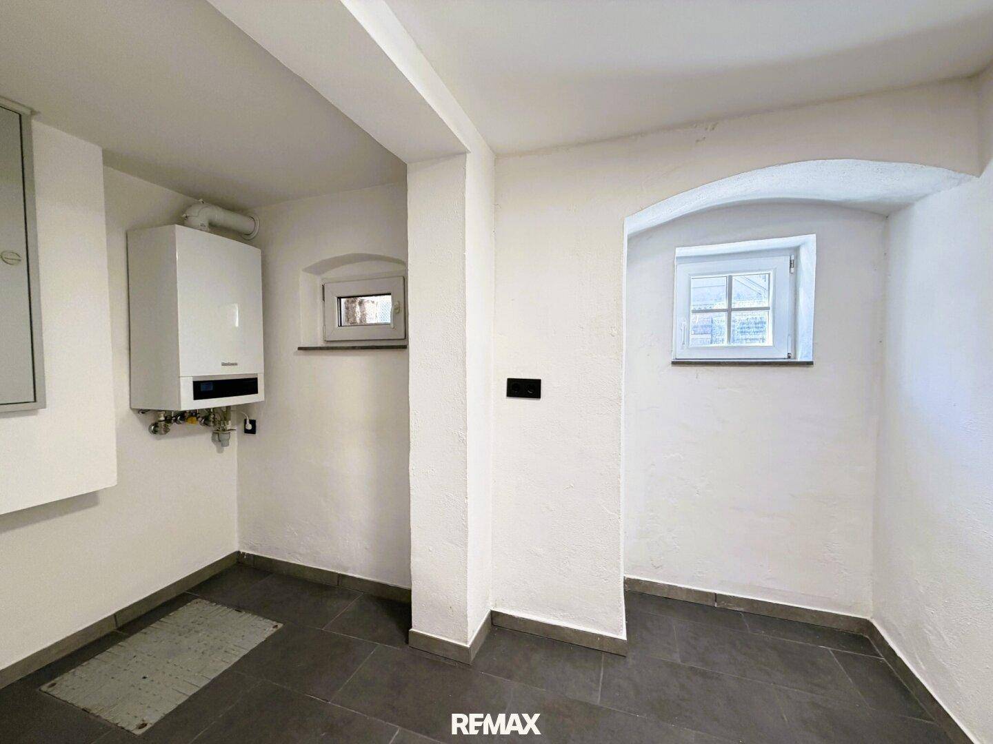 Hauswirtschaftsraum mit Heizkessel, gefliestem Boden und zwei kleinen Fenstern für Belüftung.