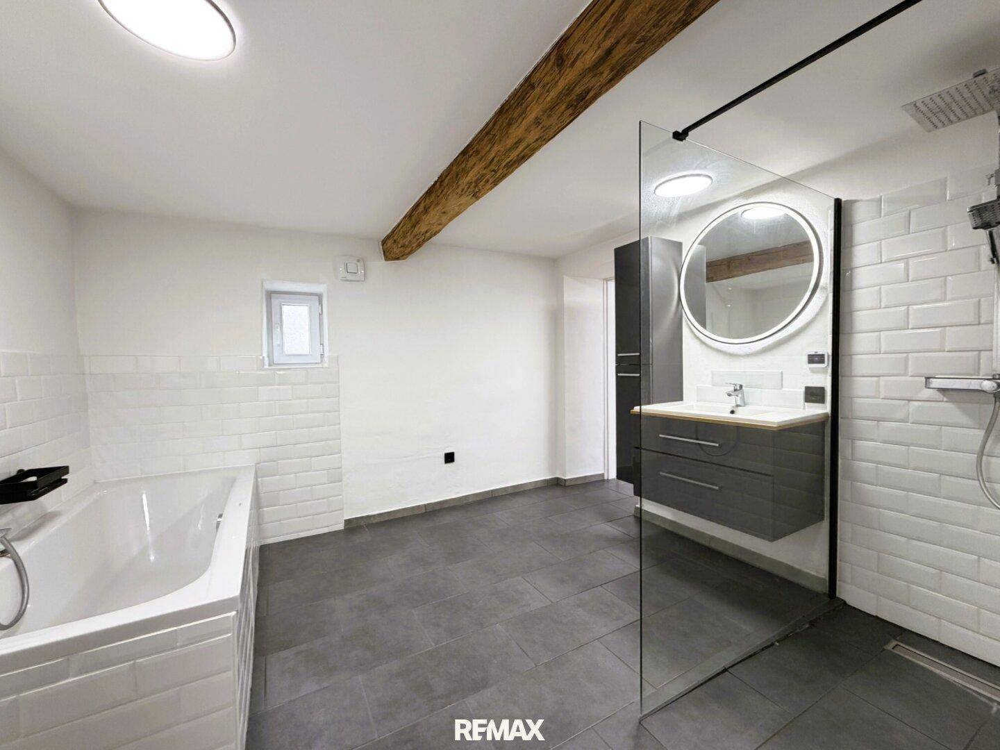 Modernes Badezimmer mit Badewanne, begehbarer Dusche, Waschtisch und sichtbarem Holzbalken.