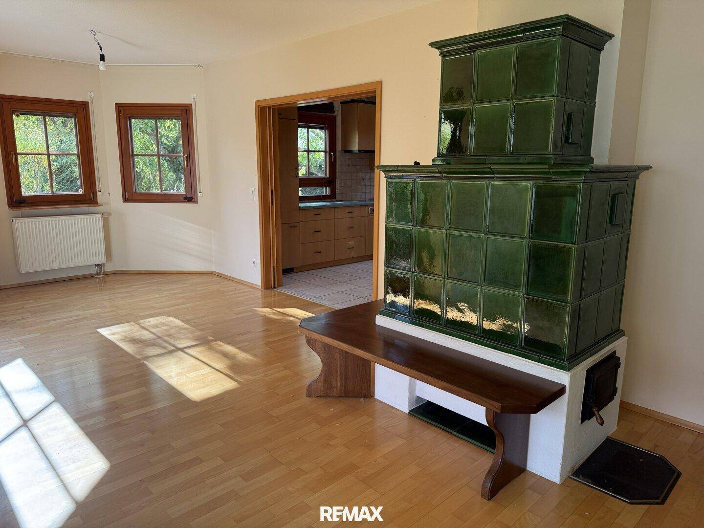Gemütliches Wohnzimmer mit traditionellem grünem Kachelofen, Parkettboden und Zugang zur Küche.