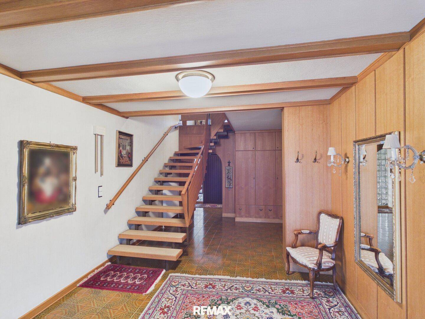 Geräumiger Flur mit Holztreppe, Holzbalkendecke und einem großen Spiegel, der den Raum erweitert.